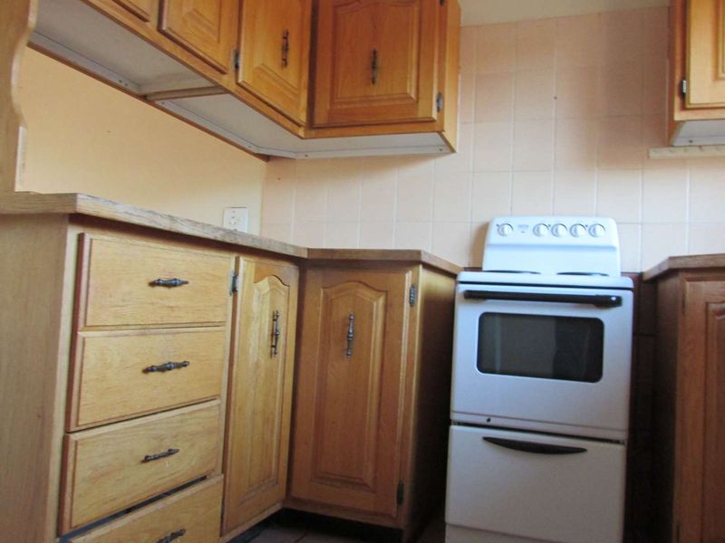 A dated kitchen featuring traditional wooden cabinetry, laminate countertops, and a tiled backsplash, offering potential for a modern renovation.