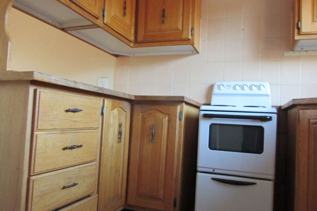 A dated kitchen featuring traditional wooden cabinetry, laminate countertops, and a tiled backsplash, offering potential for a modern renovation.