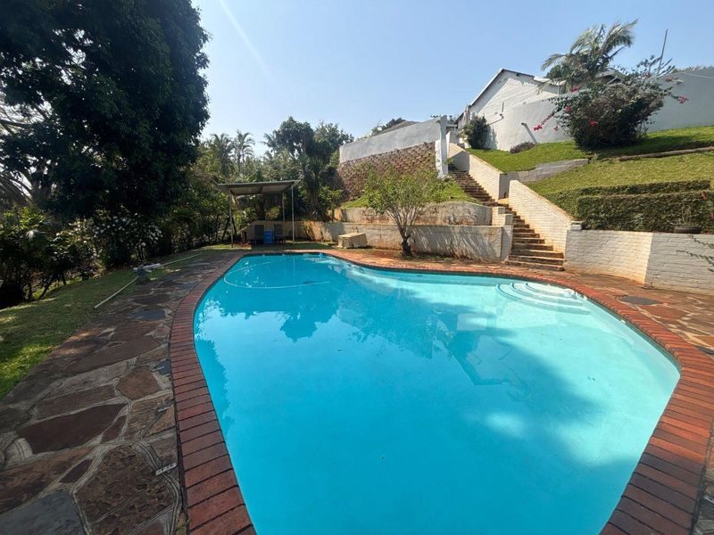 Outdoor pool area featuring a swimming pool with brick coping, stone paving, and tiered garden levels with concrete stairs.