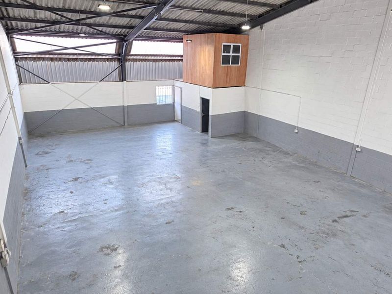 Spacious industrial warehouse unit featuring high ceilings with exposed steel trusses, concrete flooring, and a built-in mezzanine office pod.