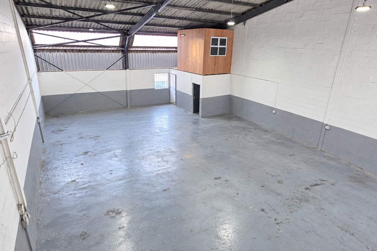 Spacious industrial warehouse unit featuring high ceilings with exposed steel trusses, concrete flooring, and a built-in mezzanine office pod.