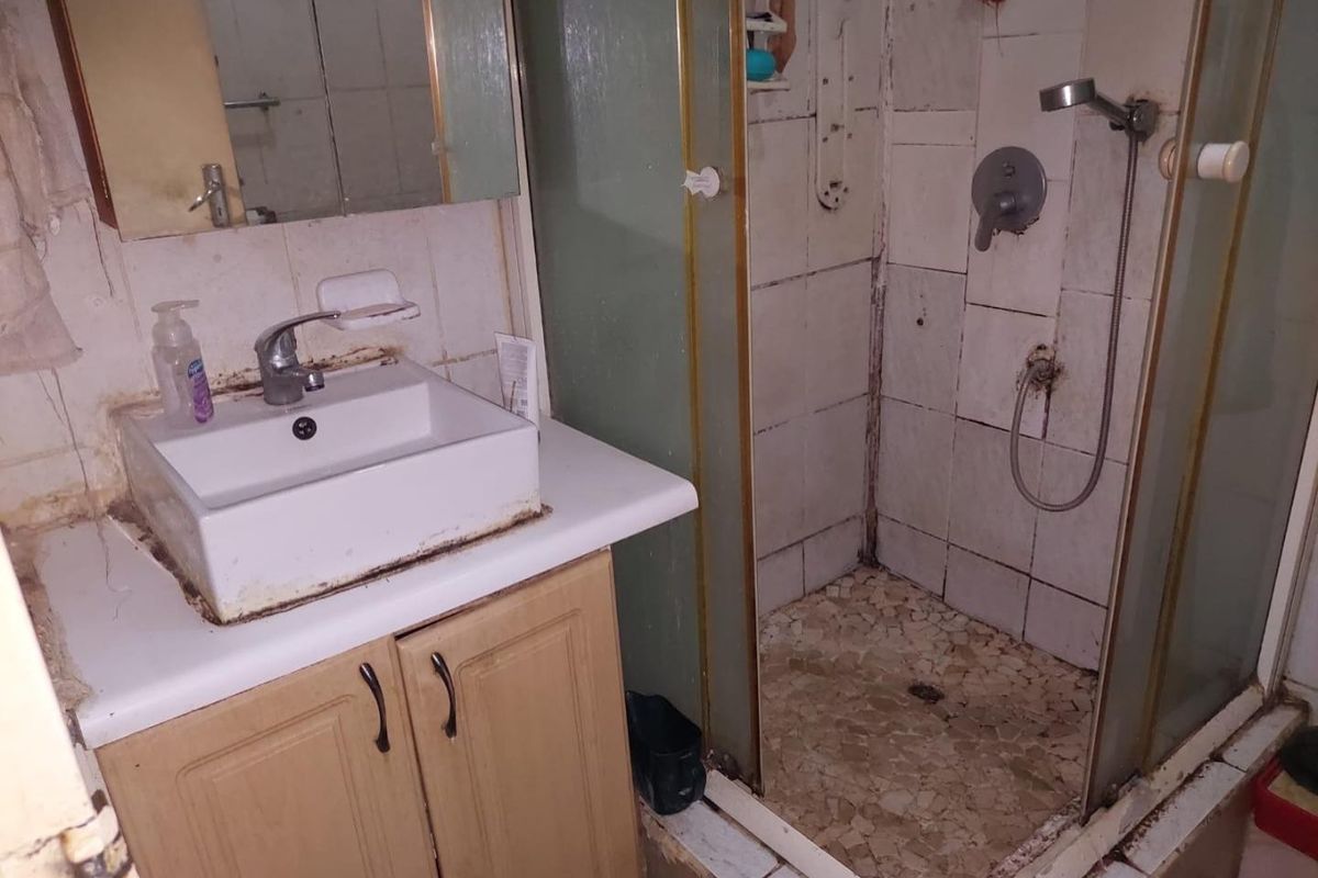 A dated bathroom featuring a vanity unit, basin, and shower enclosure, currently requiring significant maintenance and renovation to restore its functionality and aesthetic appeal.