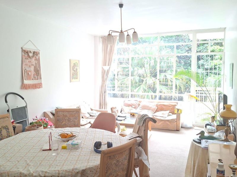 An open-plan living and dining area featuring large floor-to-ceiling windows that provide ample natural light and a view of the surrounding greenery.