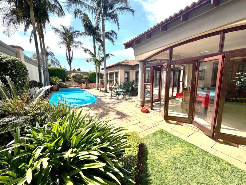 A well-maintained outdoor pool area featuring a paved patio, landscaped garden, and large bi-fold doors providing seamless indoor-outdoor flow.