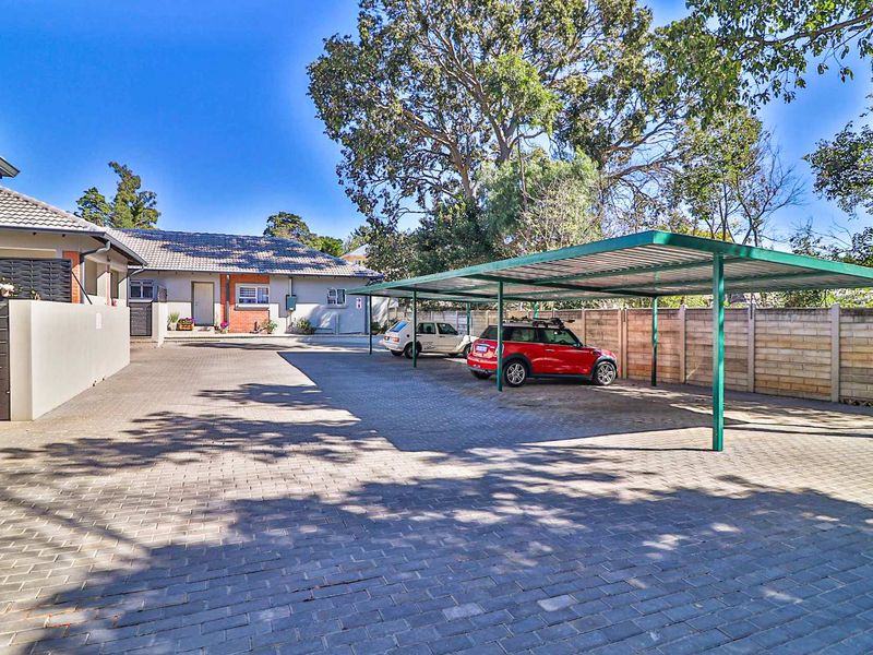 Spacious paved driveway area featuring a covered carport structure and secure boundary walling, providing ample off-street parking for the townhouse property.