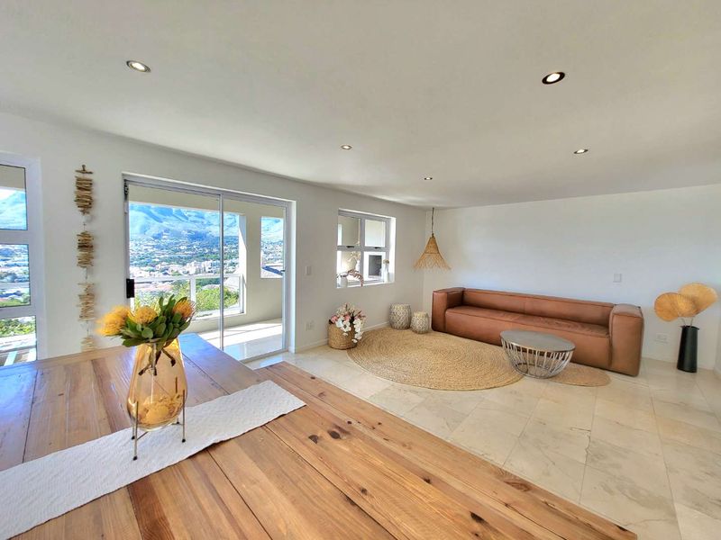 Spacious open-plan living area featuring neutral tiled flooring, recessed lighting, and large sliding doors that open to a balcony with scenic mountain views.