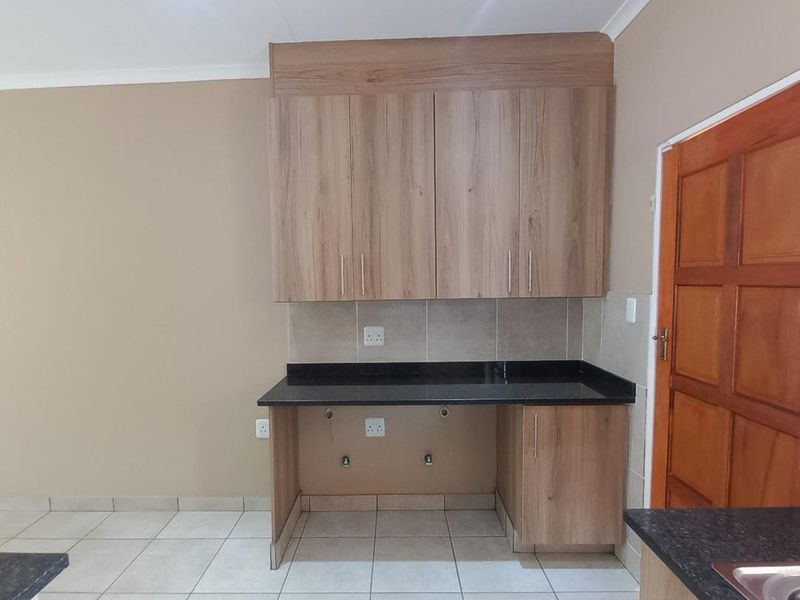 A clean, modern kitchen area featuring granite countertops, light wood-finish cabinetry, and neutral tiled flooring, providing a functional space for appliances.