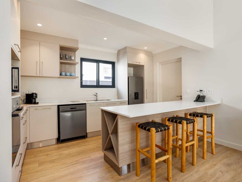 Modern kitchen featuring light-toned cabinetry, stone countertops, a functional island, and integrated appliances, finished with high-quality laminate flooring and recessed lighting.