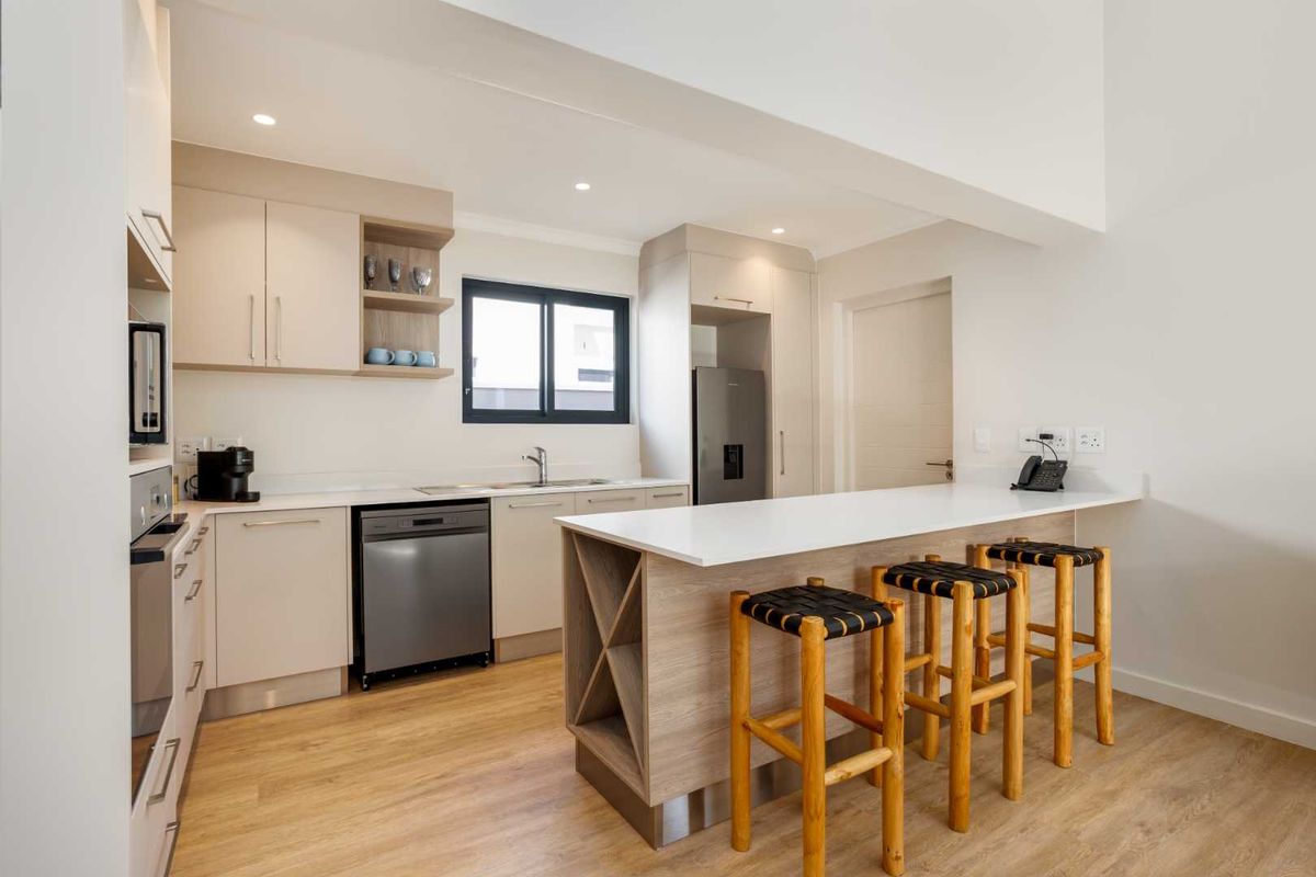 Modern kitchen featuring light-toned cabinetry, stone countertops, a functional island, and integrated appliances, finished with high-quality laminate flooring and recessed lighting.