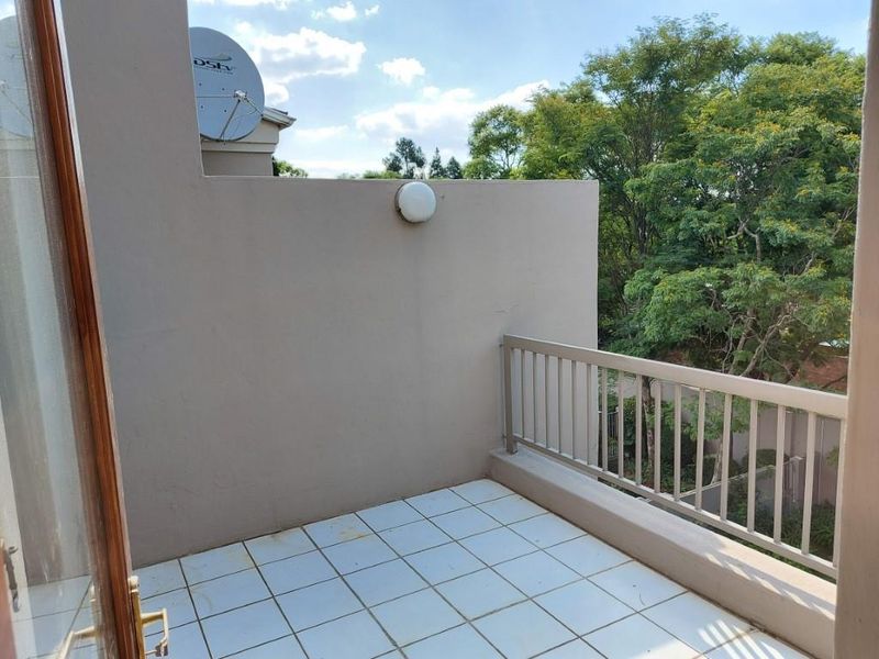 A private balcony featuring tiled flooring and a metal balustrade, offering an open outdoor space with a view of surrounding trees.