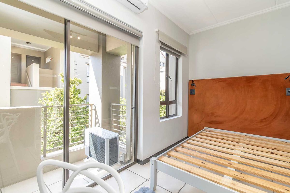 A bright bedroom featuring tiled flooring, a built-in headboard, air conditioning unit, and sliding glass doors leading to a private balcony.