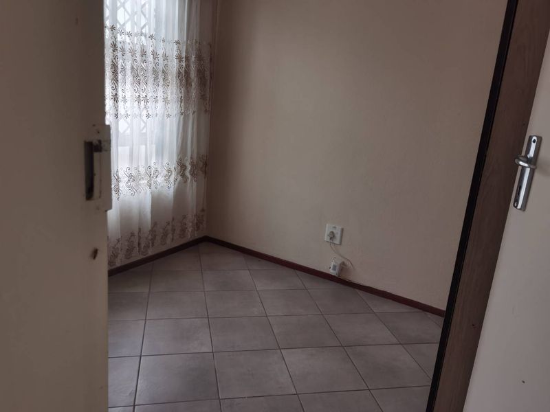An empty bedroom featuring neutral wall paint, tiled flooring, and a window fitted with a security gate.
