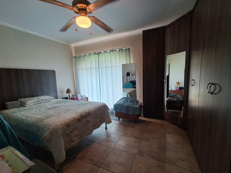 Spacious bedroom featuring tiled flooring, a ceiling fan, and extensive built-in cupboard storage with an integrated mirror.