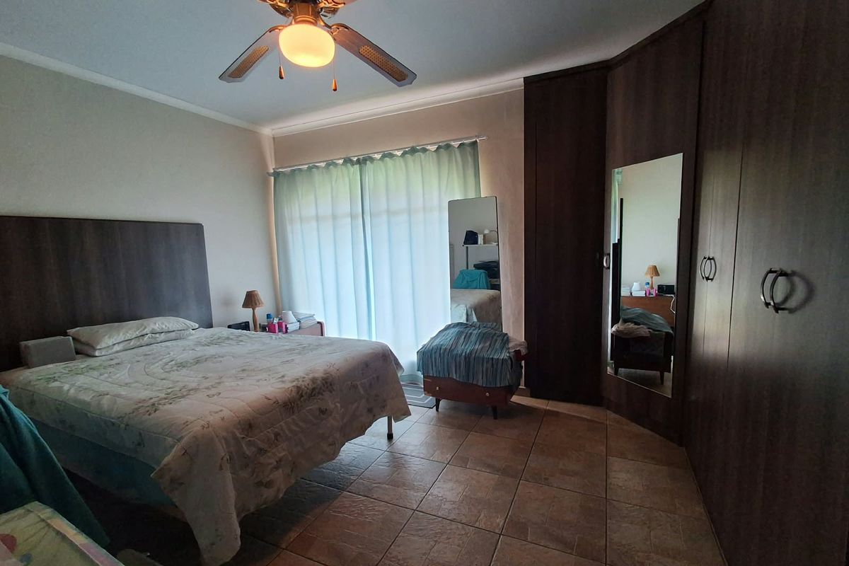 Spacious bedroom featuring tiled flooring, a ceiling fan, and extensive built-in cupboard storage with an integrated mirror.