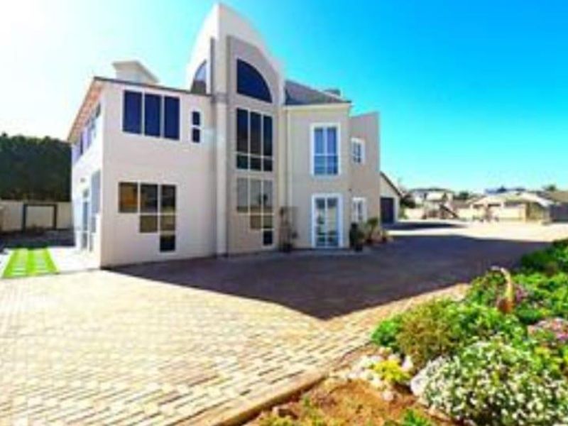 A modern multi-level residential property featuring a paved driveway, expansive feature windows, and well-maintained landscaped garden beds.