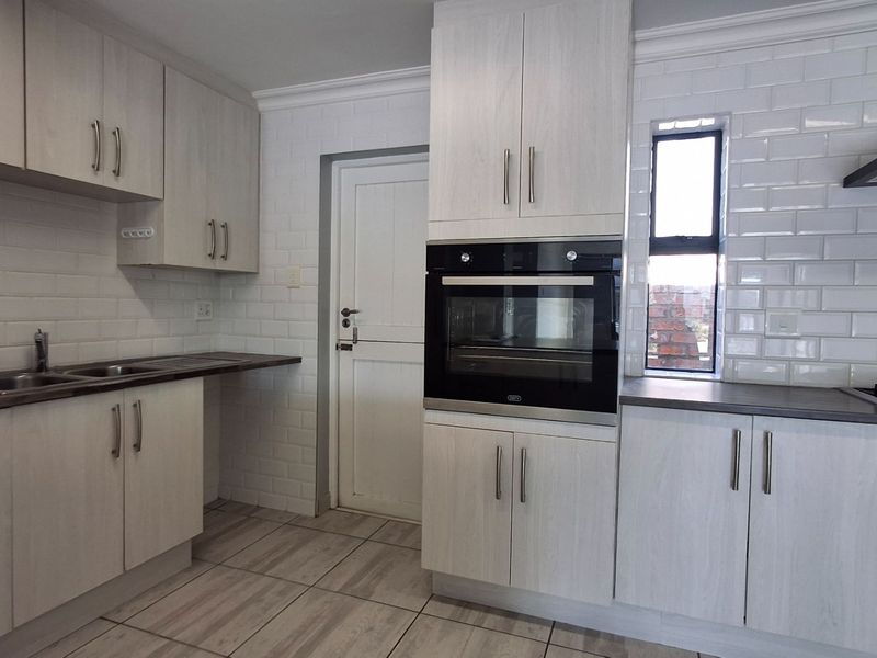 Modern kitchen featuring light wood-grain cabinetry, subway tile backsplash, built-in oven, extractor fan, and dark laminate countertops with tiled flooring.