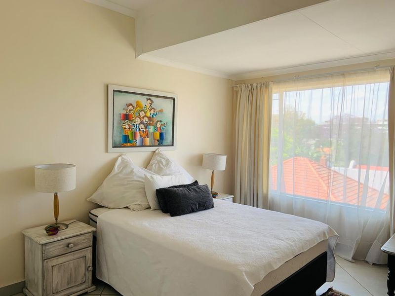 A well-lit bedroom featuring tiled flooring and a large window with natural light, offering a comfortable and functional living space.