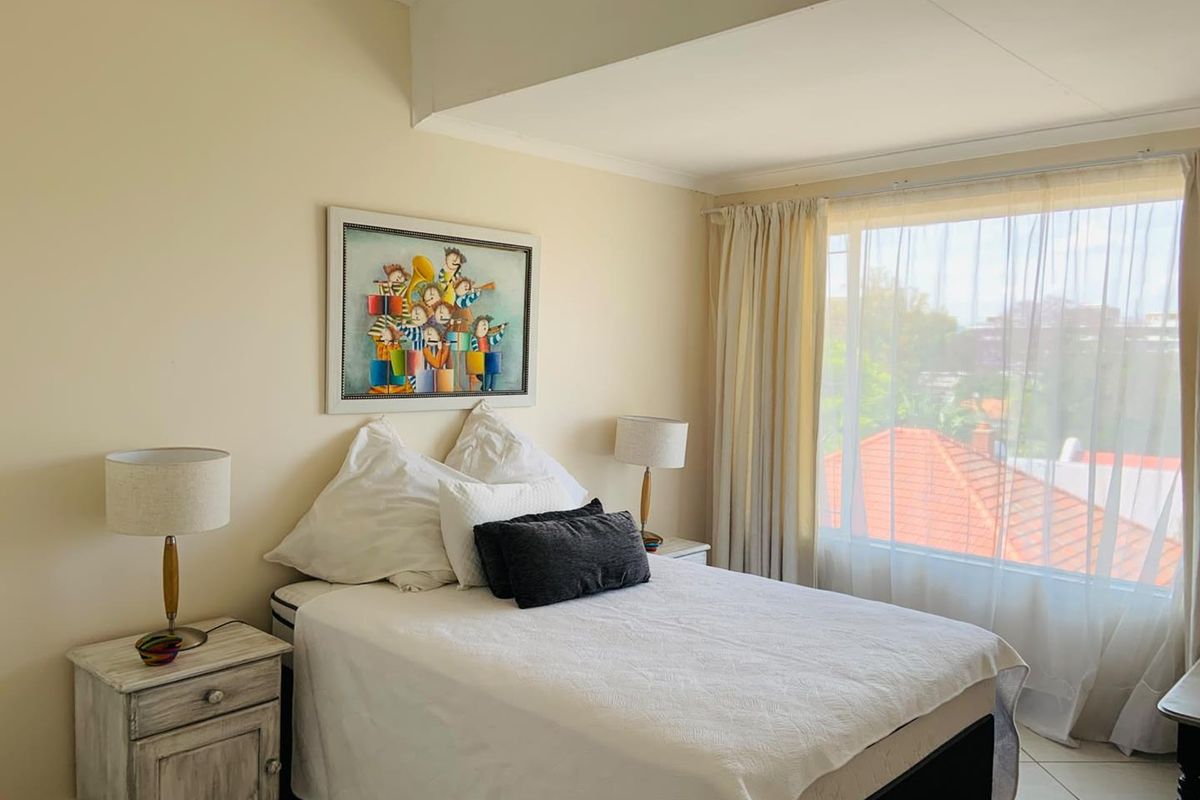 A well-lit bedroom featuring tiled flooring and a large window with natural light, offering a comfortable and functional living space.