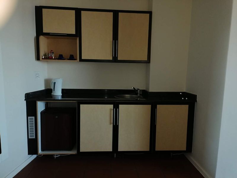 A compact kitchenette featuring built-in cabinetry, a stone countertop, and a stainless steel sink, currently showing signs of wear and missing cabinet components.
