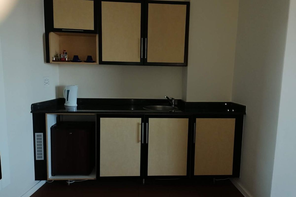 A compact kitchenette featuring built-in cabinetry, a stone countertop, and a stainless steel sink, currently showing signs of wear and missing cabinet components.