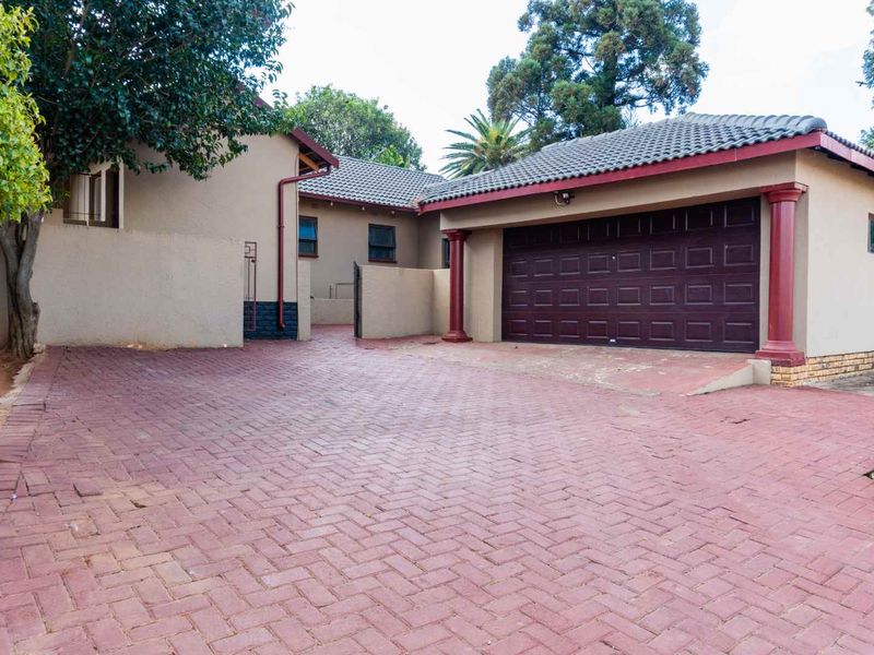 Front exterior view of the property featuring a paved driveway, double garage with dark doors, and plastered walls with decorative columns.