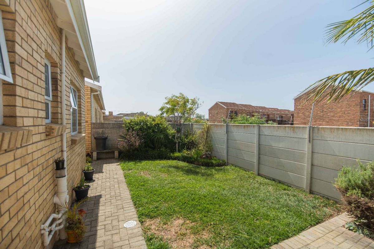 A private rear garden featuring a paved walkway, small lawn area, and concrete boundary walling.