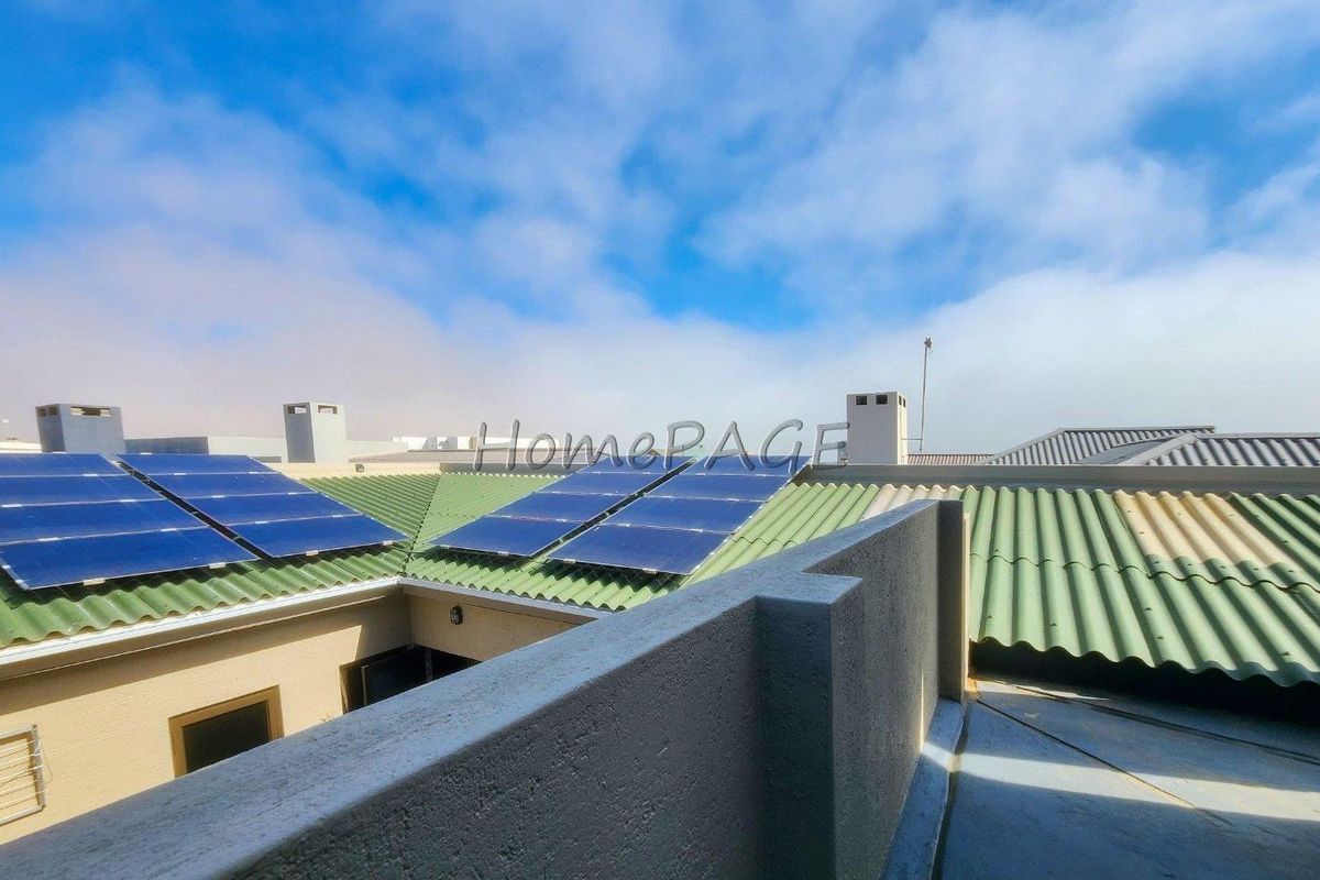An elevated view of the property roofline featuring installed solar panels, green corrugated roofing, and chimney stacks under a clear sky.