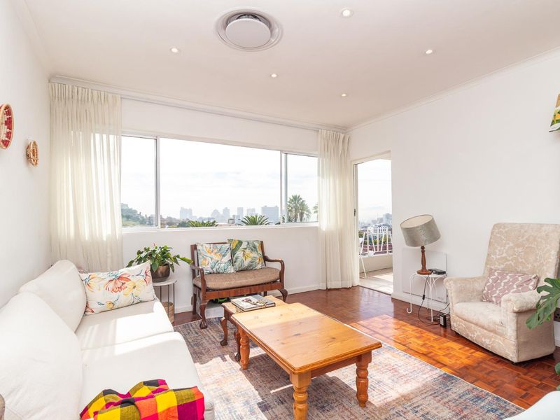 Bright living room featuring classic parquet flooring, recessed lighting, and large windows providing natural light and access to an adjoining balcony.