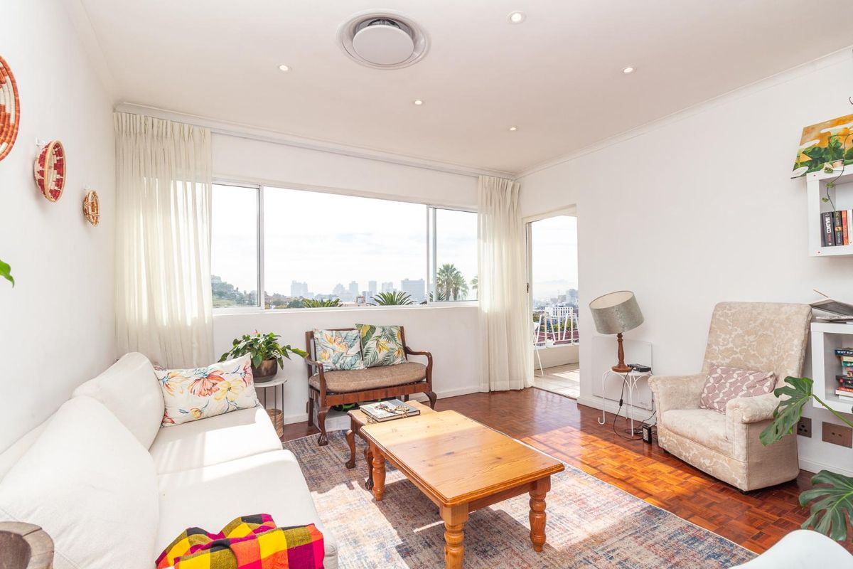 Bright living room featuring classic parquet flooring, recessed lighting, and large windows providing natural light and access to an adjoining balcony.