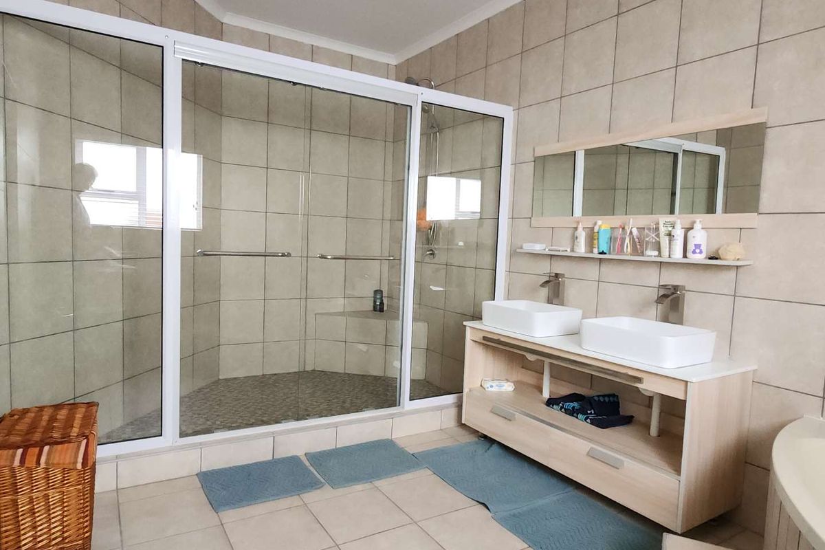 A well-maintained bathroom featuring a large walk-in glass shower, double vanity with vessel sinks, and neutral floor-to-ceiling tiling.