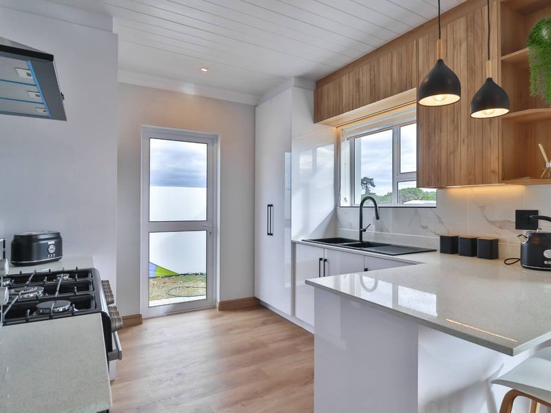 Modern kitchen featuring sleek white cabinetry, timber-look accents, stone countertops, a gas hob, and high-quality finishes with direct access to the exterior.