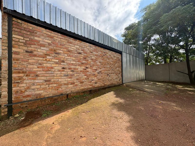 Rear exterior view featuring a combination of exposed brick and corrugated metal cladding with a paved area and boundary wall.