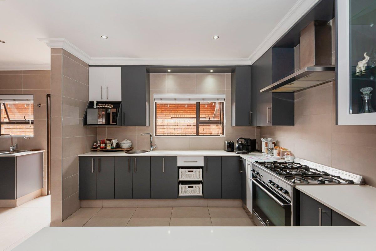 Modern kitchen featuring dark cabinetry, stone countertops, tiled backsplash, and a built-in gas stove with an extractor fan.