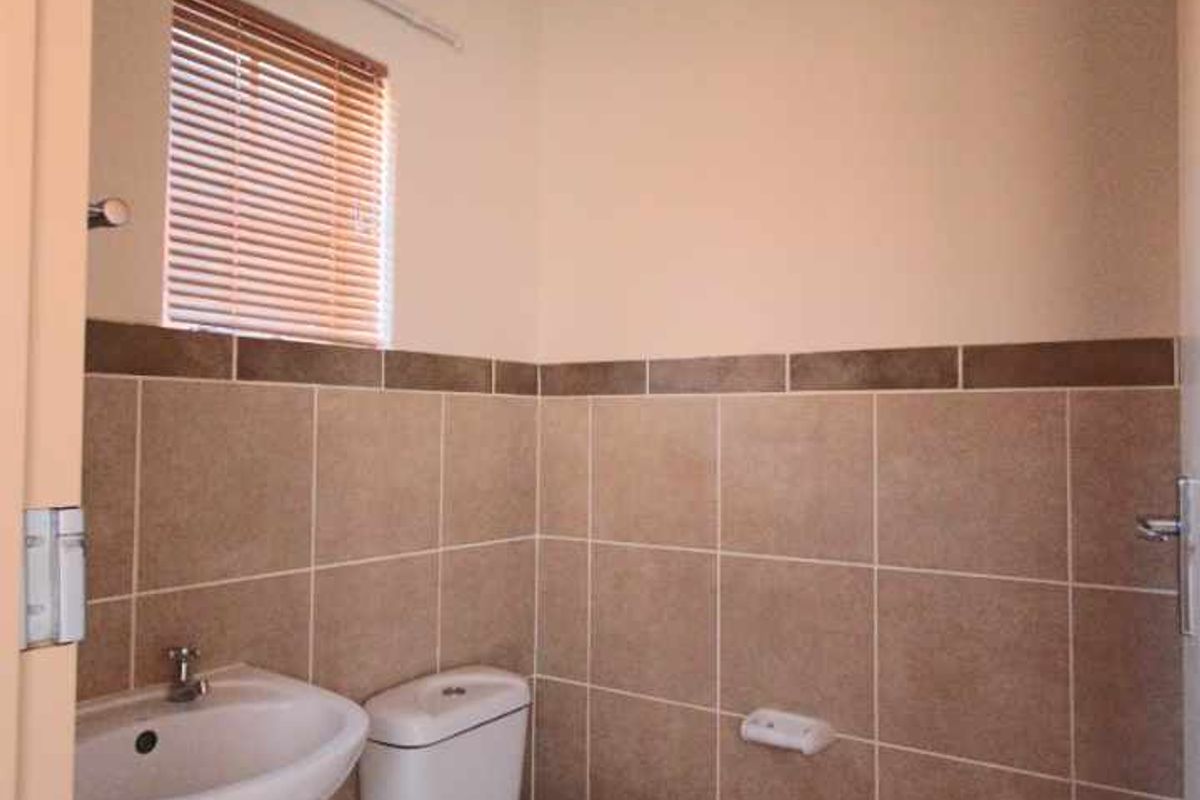 A compact guest bathroom featuring a pedestal basin, a standard toilet, and neutral wall tiling.