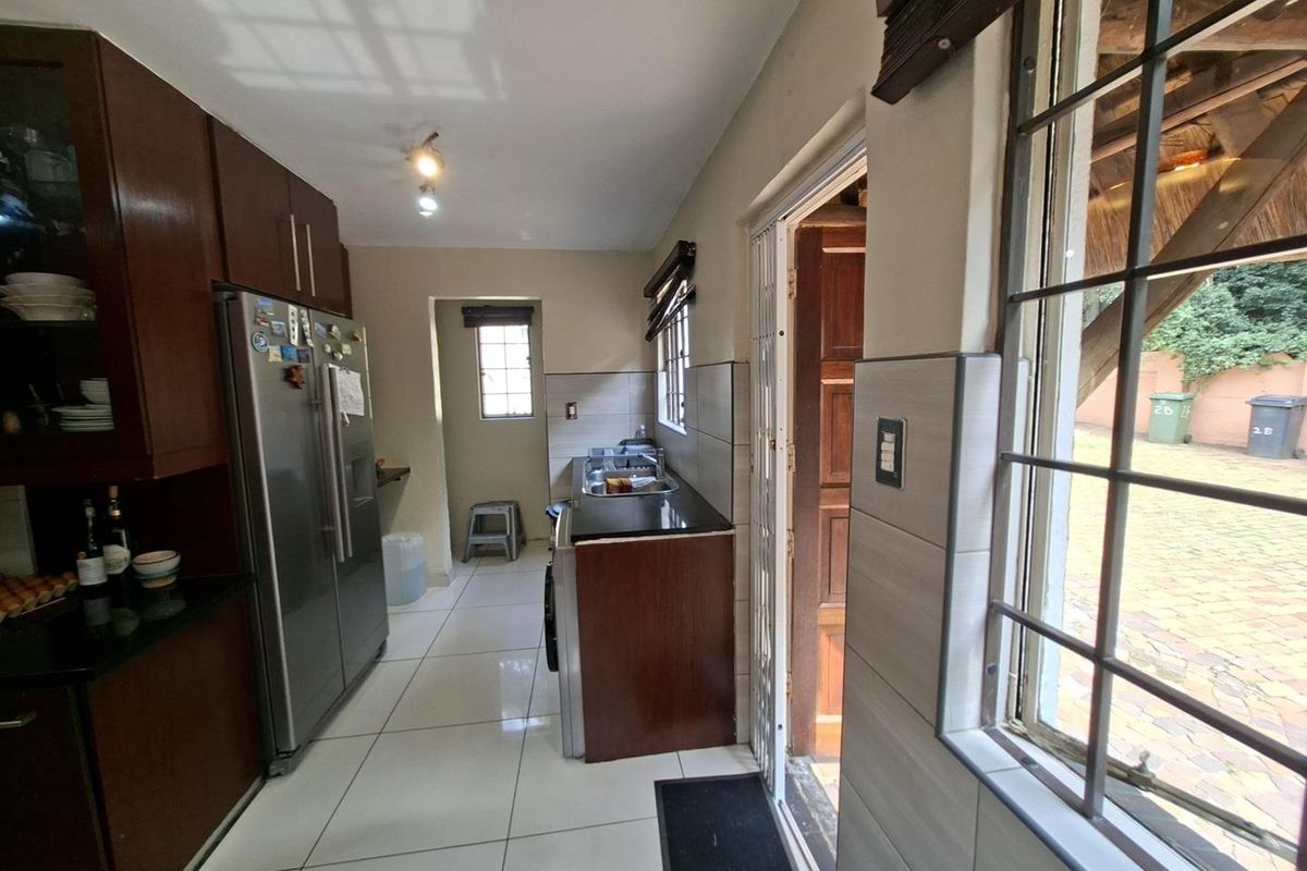 A functional kitchen featuring dark wood cabinetry, granite countertops, stainless steel sink, and tiled flooring with direct access to the exterior.