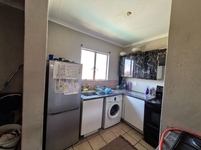 Compact kitchen featuring tiled flooring, laminate countertops, built-in cabinetry, and integrated appliances, offering a functional layout with potential for cosmetic updates.