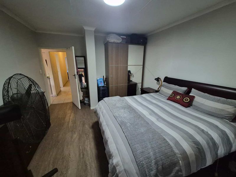A functional bedroom featuring laminate flooring, a built-in wardrobe, and access to an adjacent hallway.