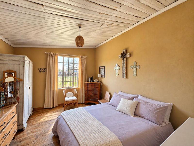 A bedroom featuring timber plank ceilings, original timber flooring, and a grid-pattern window, offering a rustic aesthetic with potential for modern updates.