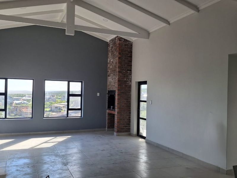 Spacious living area featuring a vaulted ceiling with exposed beams, a brick fireplace, and large windows offering natural light and scenic views.