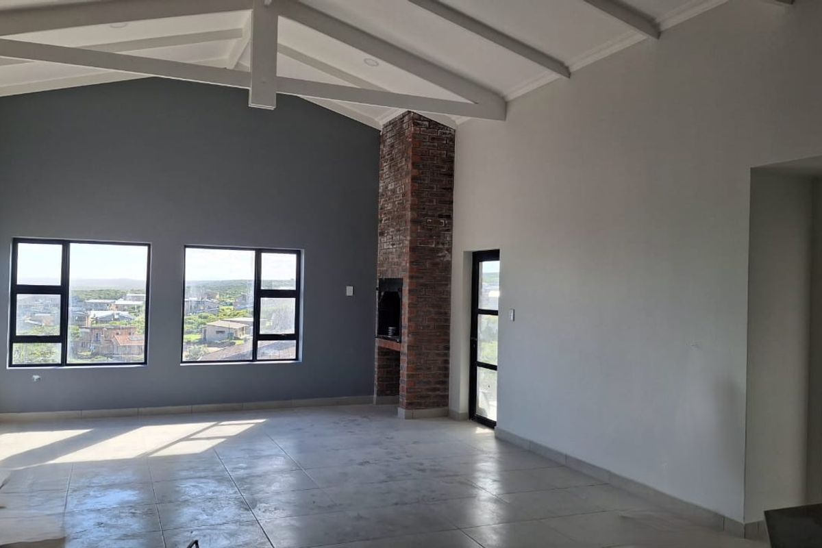 Spacious living area featuring a vaulted ceiling with exposed beams, a brick fireplace, and large windows offering natural light and scenic views.