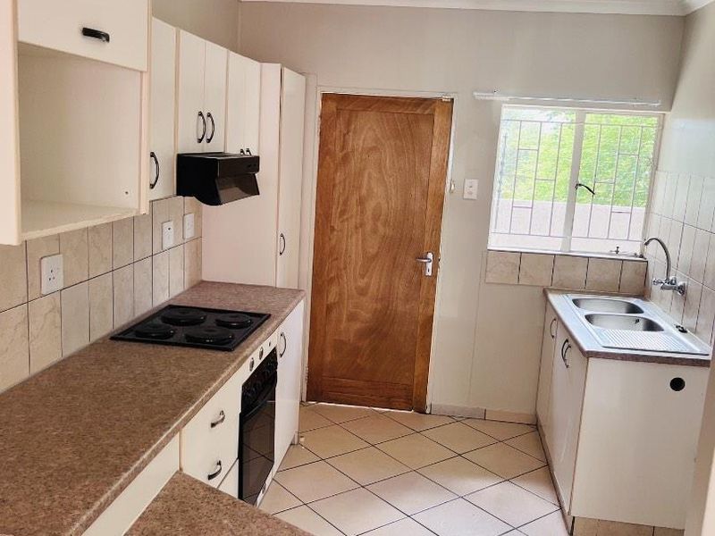 A functional kitchen featuring laminate countertops, built-in oven with hob, extractor fan, and double bowl sink with tiled splashbacks and ceramic flooring.