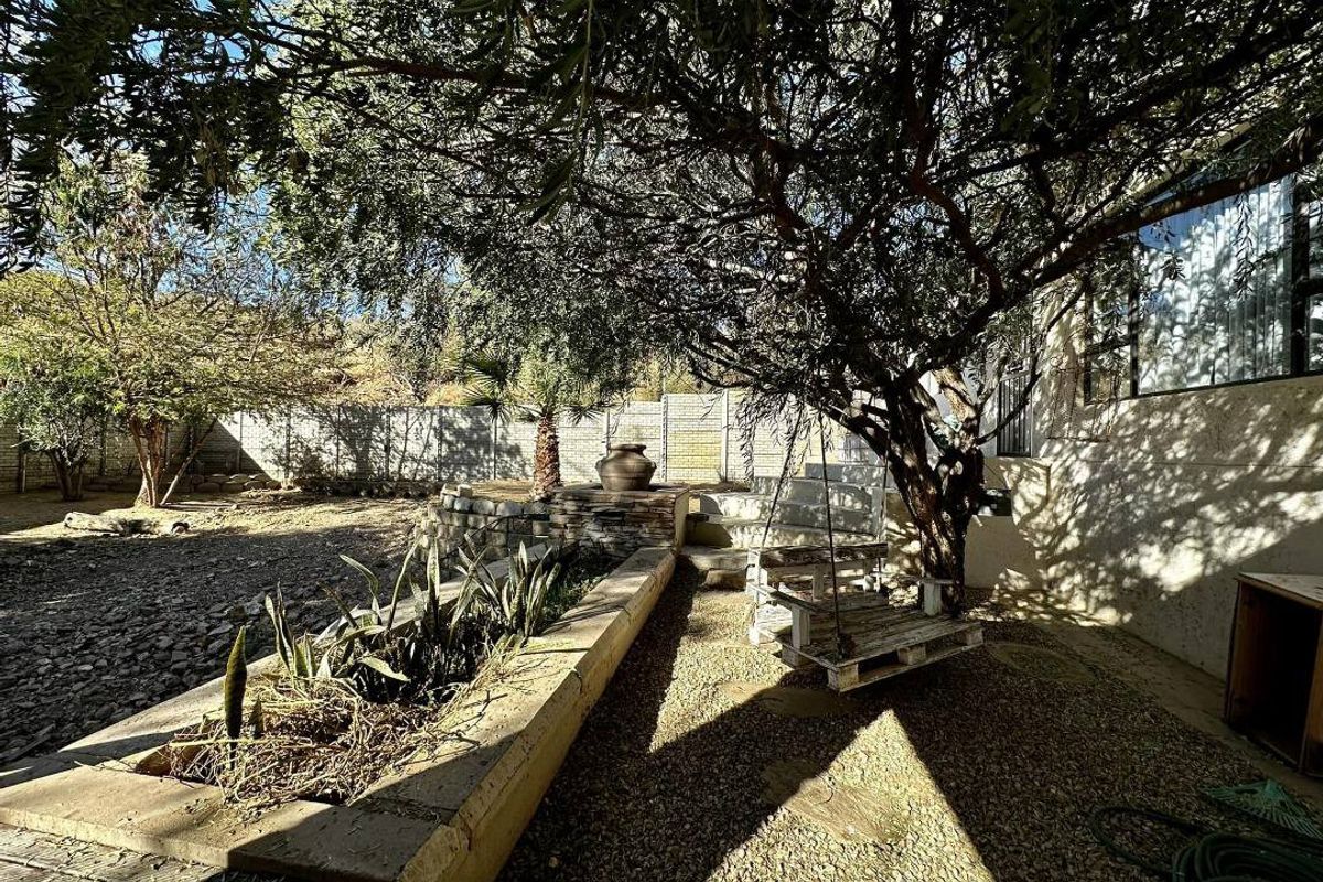 A rear garden area featuring a stone retaining wall, mature trees, and gravel landscaping, providing a shaded outdoor space.