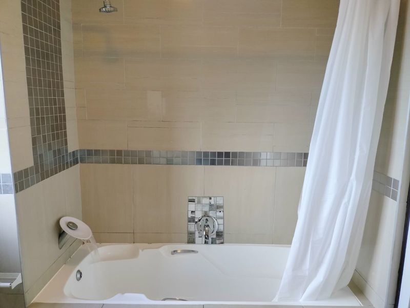 A clean bathroom featuring a built-in bathtub with a shower head, complemented by neutral wall tiles and a decorative mosaic accent strip.