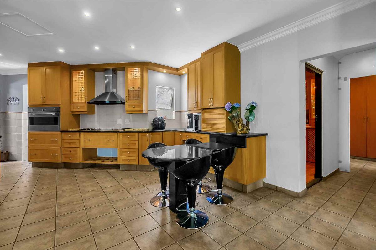 Spacious kitchen featuring wooden cabinetry, built-in oven, extractor fan, and tiled flooring, offering a functional layout with an integrated breakfast bar area.