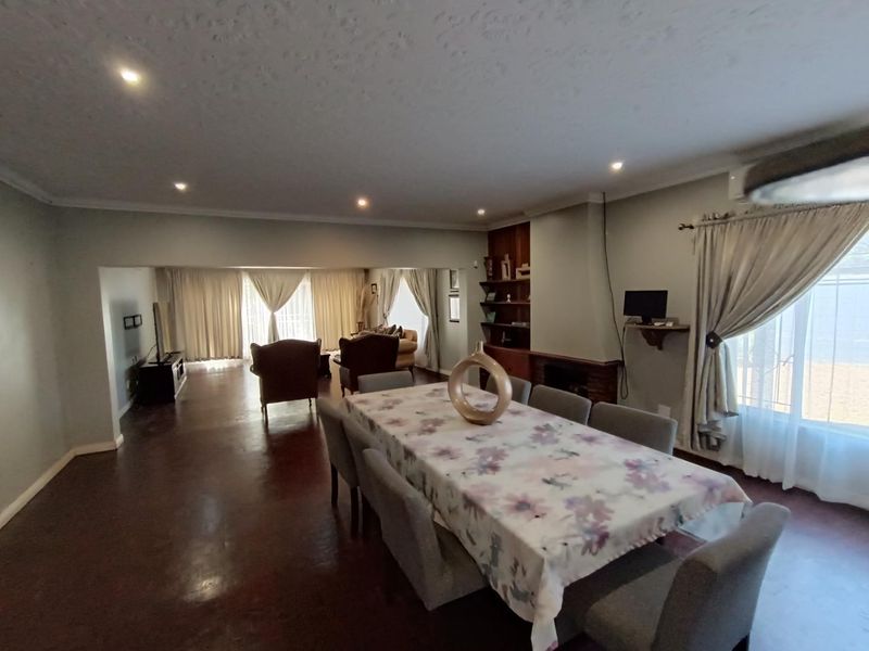 Spacious open-plan living and dining area featuring a fireplace, built-in shelving, recessed lighting, and large windows with natural light.