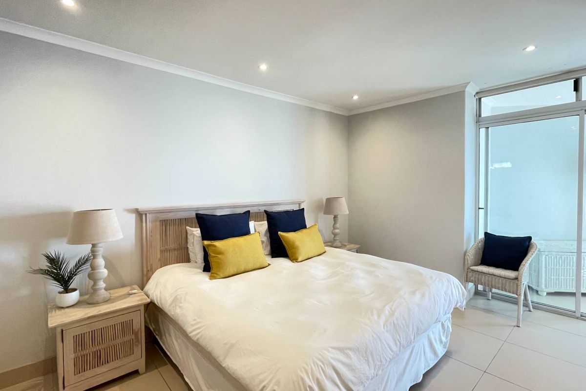 A bright and spacious bedroom featuring neutral tiled flooring, recessed downlighting, and a large sliding glass door providing access to the balcony.