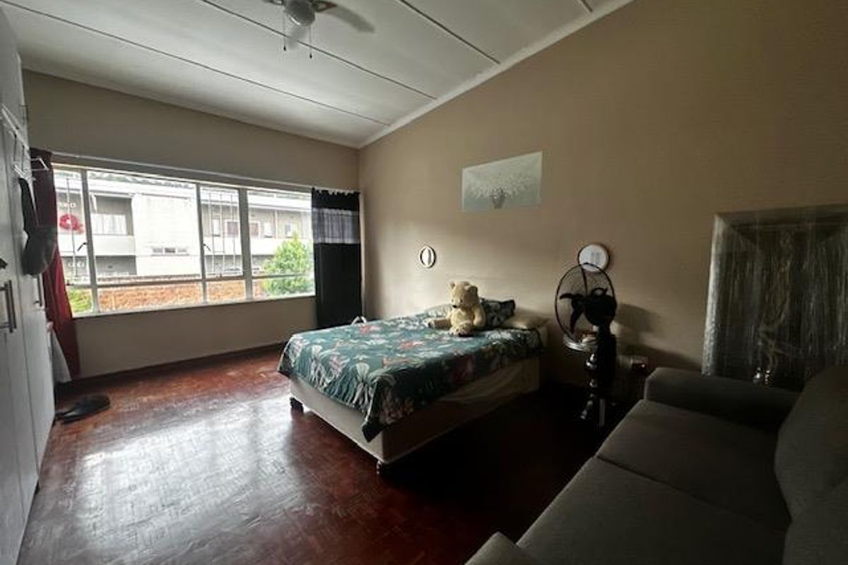 A spacious bedroom featuring parquet flooring, a ceiling fan, and large windows that provide ample natural light.