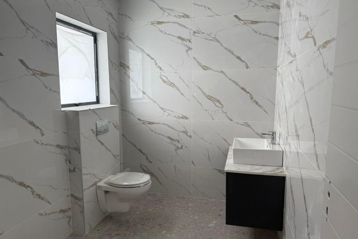 Modern bathroom featuring floor-to-ceiling marble-look wall tiles, a wall-mounted toilet with concealed cistern, and a contemporary floating vanity with a vessel sink.