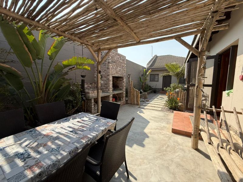 Outdoor patio area featuring a rustic timber pergola, built-in brick braai, and concrete flooring, providing a functional space for outdoor entertaining.