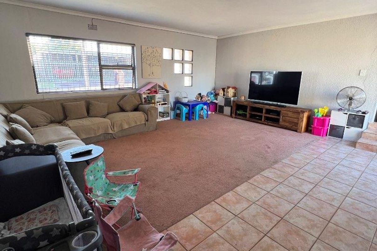 Spacious living room featuring a combination of carpet and tiled flooring, large windows, and a neutral wall finish.